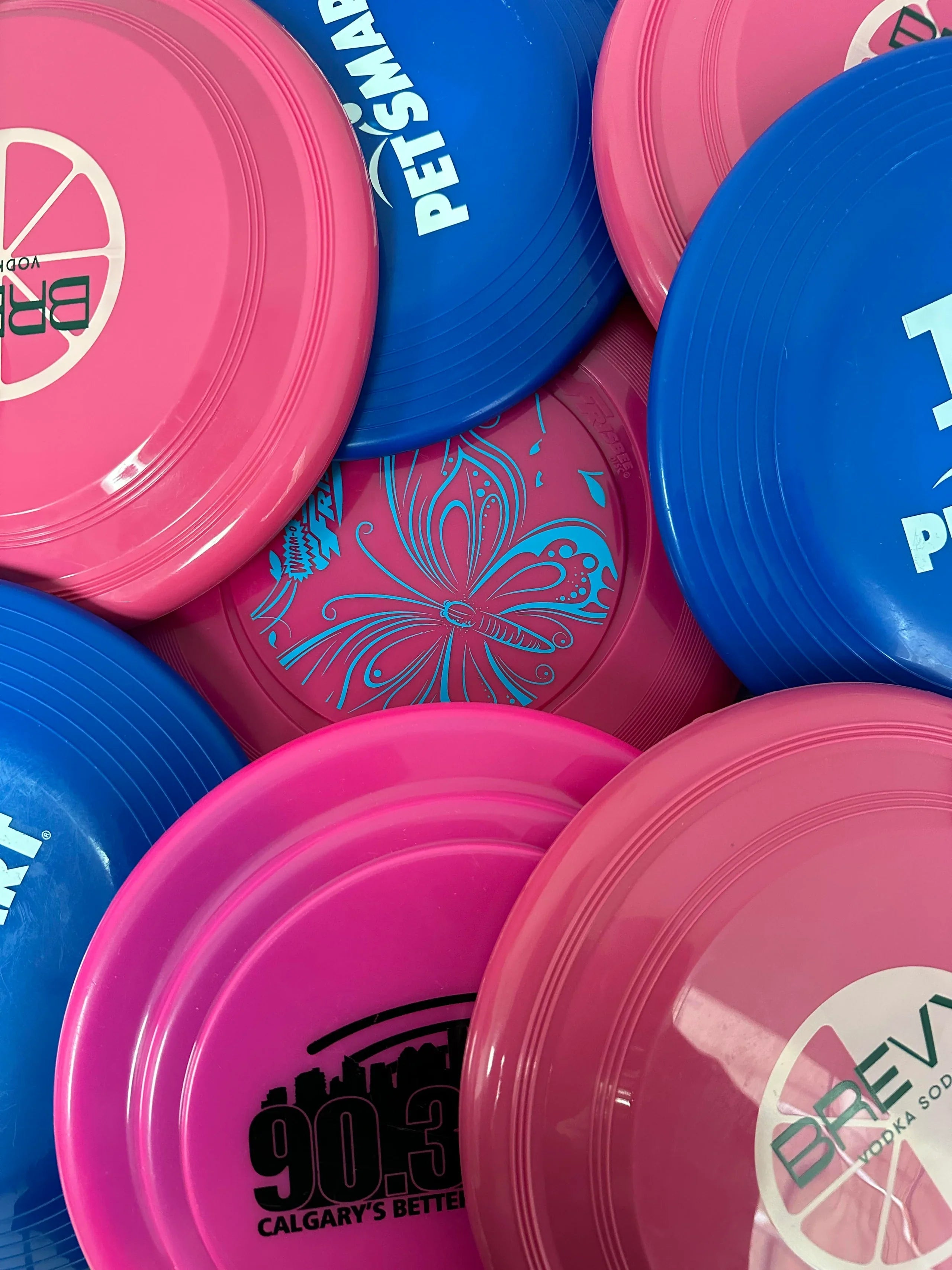 Stack of pink and blue frisbees with various designs and text.