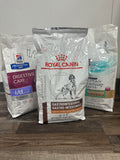 Three bags of Royal Canin veterinary diet products on a wooden surface.